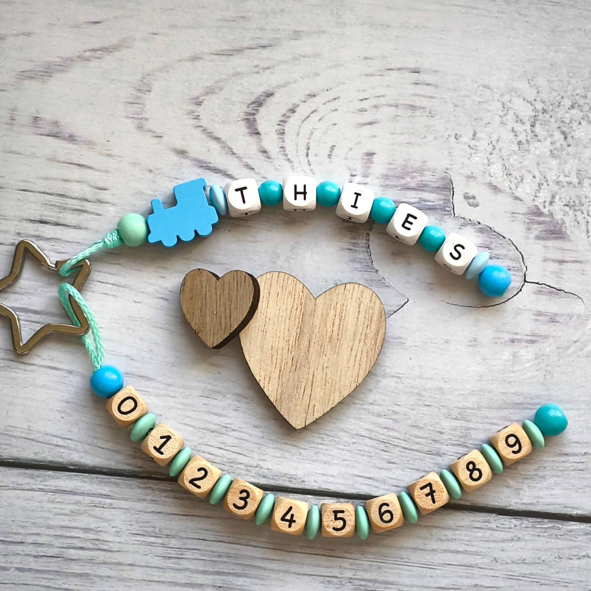 Notfallkette mit Name und Telefonnumemr aus Holzperlen in Natur, Weiß und Blau, mit Motivvperle Lok und einem Stern als Schlüsselring Notfallkette mit Name und Telefonnumemr aus Holzperlen in Natur, Weiß und Blau, mit Motivvperle Lok und einem Stern als Schlüsselring